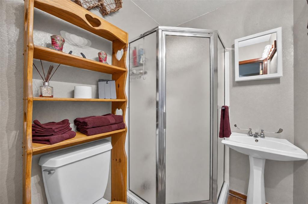 10964 River Ranch Road Kemp, TX 75143 - Photo 25 of 40 Corner shower with frosted glass enclosure, pedestal sink, wall-mounted mirror, and wood shelving unit