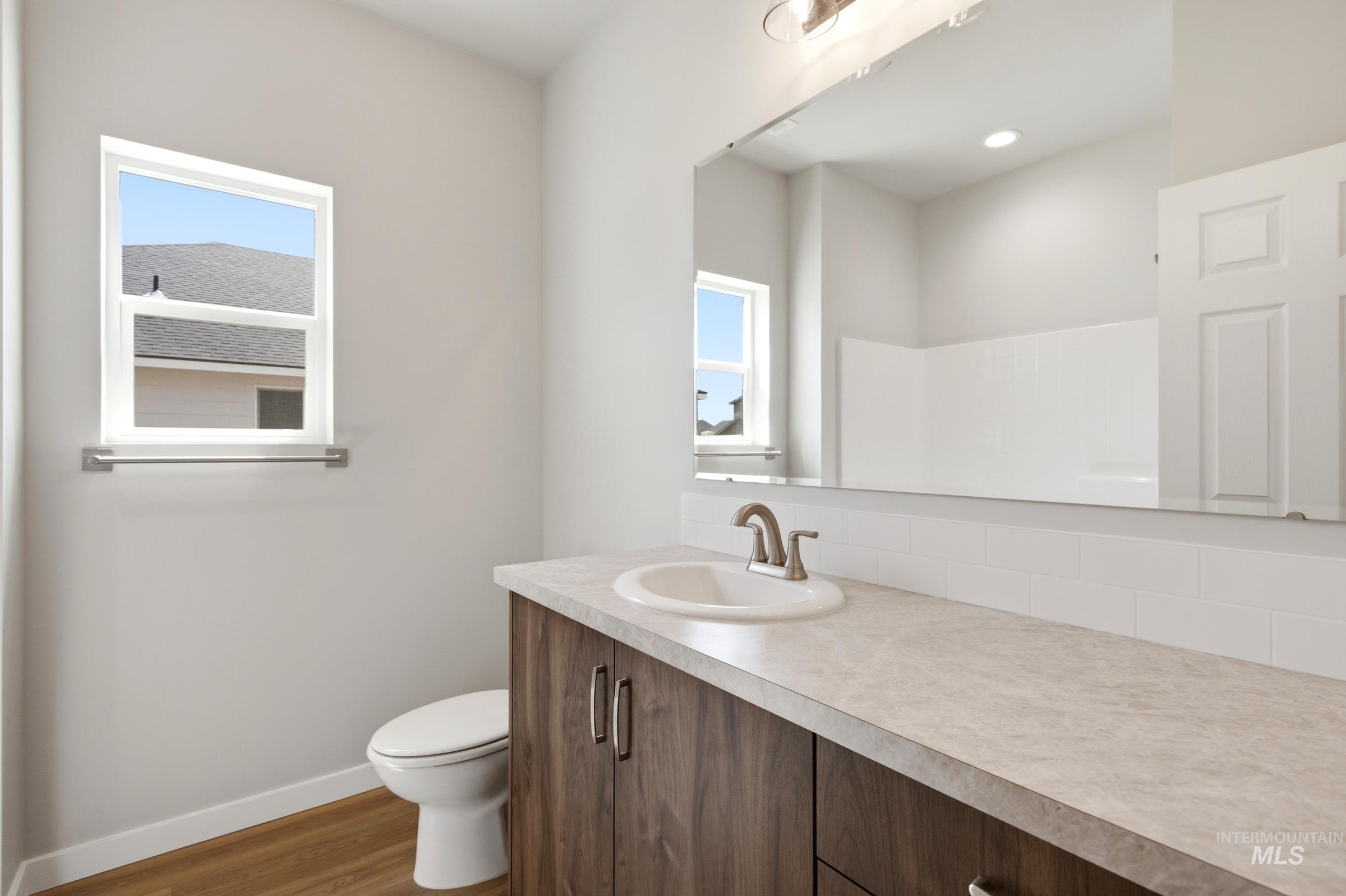 509 Waverly Avenue Middleton, ID 83644 - Photo 13 of 19 Bathroom featuring a wood-finish vanity with integrated sink, a neutral countertop, an expansive wall-mounted mirror, and wood-finish flooring