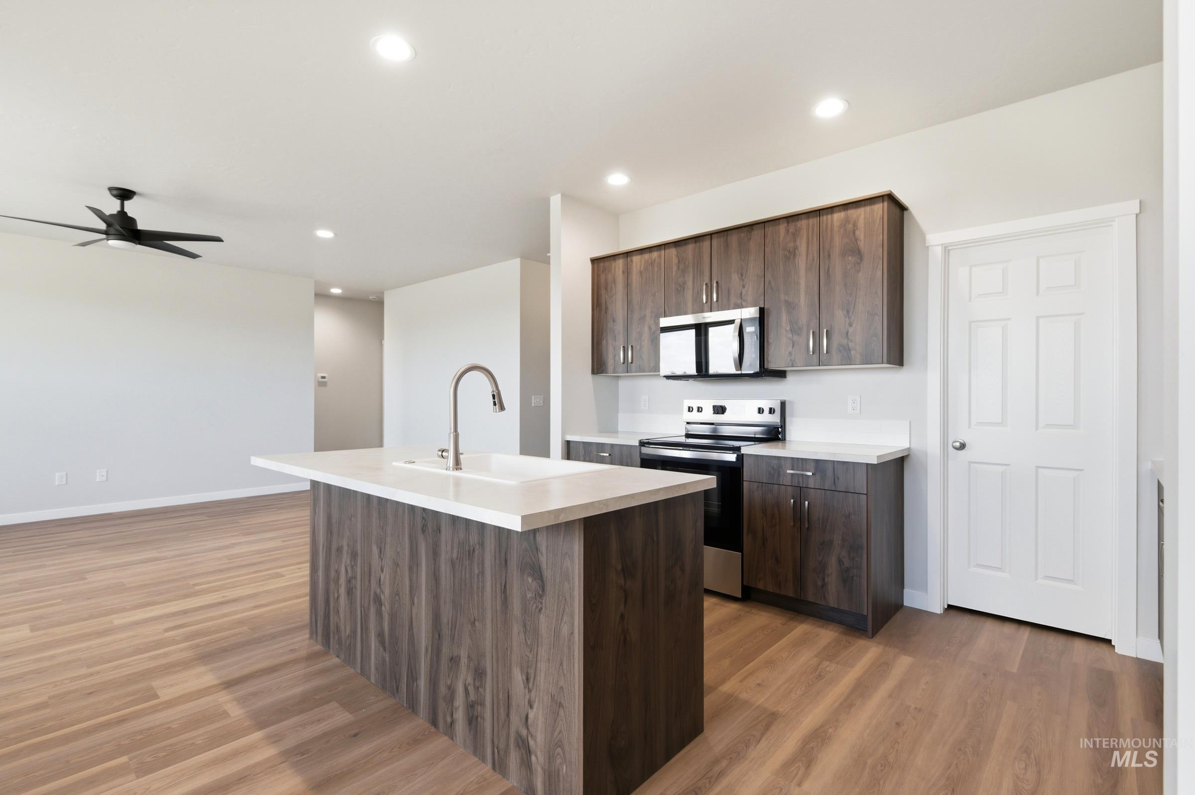509 Waverly Avenue Middleton, ID 83644 - Photo 6 of 19 Kitchen island with an undermount sink and gooseneck faucet, light-toned countertops, wood-finish flooring, recessed lighting, and a dark wood-finish cabinetry