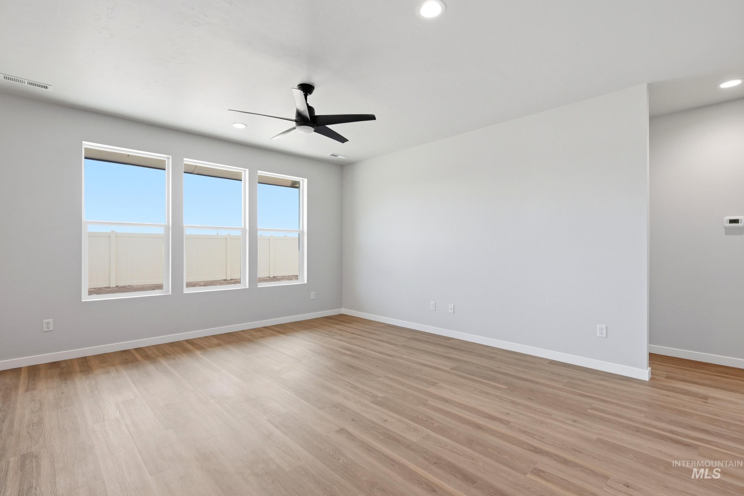 509 Waverly Avenue Middleton, ID 83644 - Photo 8 of 19 Spacious room featuring three large windows, light wood-finish flooring, a modern black ceiling fan, recessed lighting, and crisp white baseboards