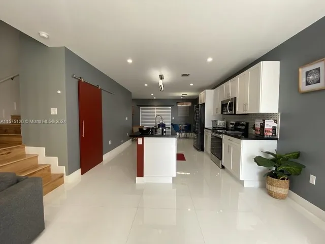a living room with stainless steel appliances furniture a rug and a kitchen view