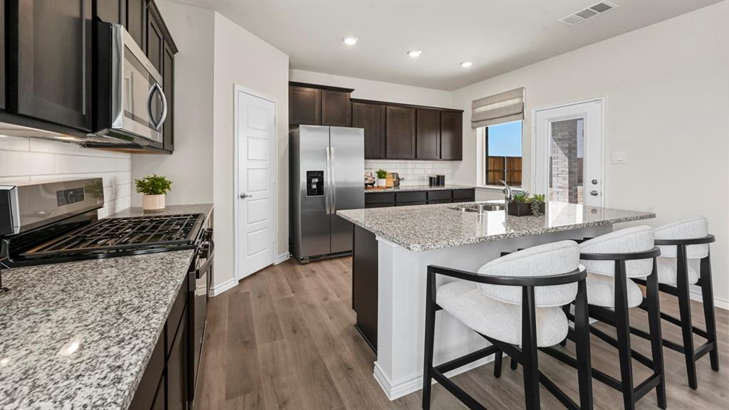 1305 Rusted Rail Drive Princeton, TX 75407 - Photo 21 of 35 a kitchen with stainless steel appliances granite countertop a stove top oven a refrigerator a sink and a dining table with wooden floor