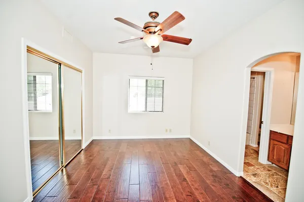 an empty room with wooden floor fan and windows