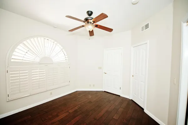 an empty room with wooden floor fan and windows