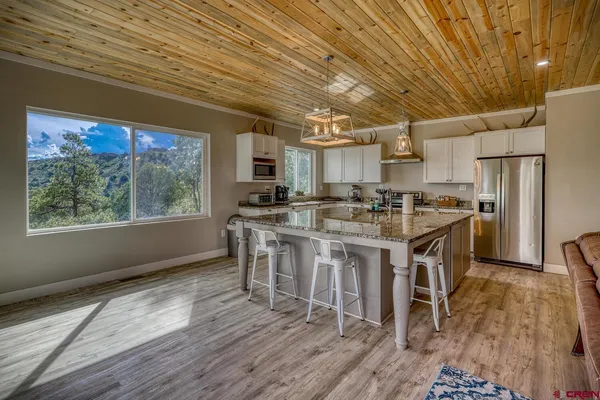 a kitchen with stainless steel appliances granite countertop a stove a refrigerator a sink a dining table and chairs with wooden floor