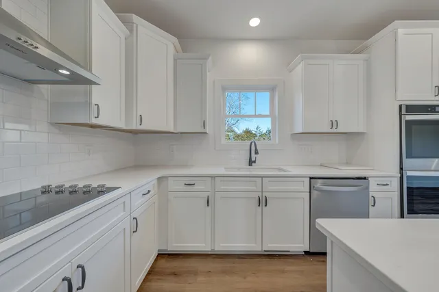 a kitchen with a sink dishwasher and white cabinets with wooden floor