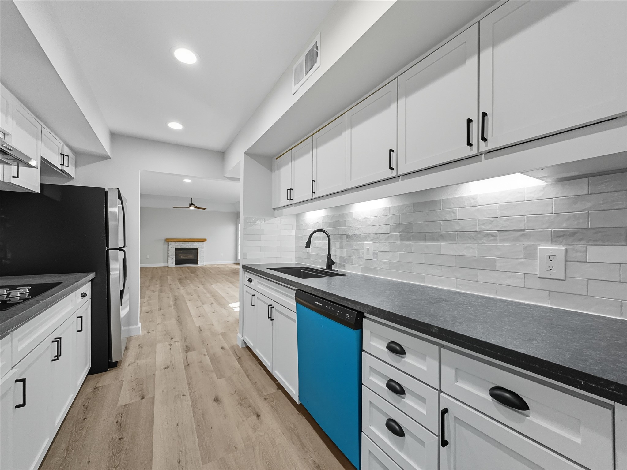2243 West Alabama Street, Unit 10 Houston, TX 77098 - Photo 12 of 45 Modern kitchen with sleek white cabinetry, dark countertops, and stainless steel appliances. The space features a stylish tile backsplash and recessed lighting. The open layout leads into a living area with wood flooring and a fireplace, creating a warm and inviting atmosphere.