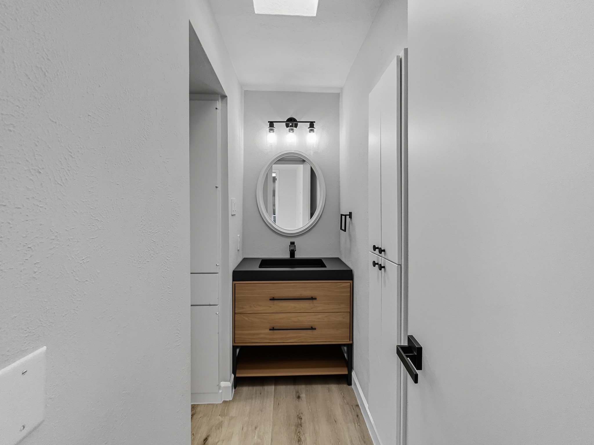 2243 West Alabama Street, Unit 10 Houston, TX 77098 - Photo 23 of 45 Modern primary bathroom with a sleek design. It features a wooden vanity with a black countertop and sink, a round mirror, and stylish lighting. The space is compact and has a bright, neutral color palette enhancing its contemporary feel.