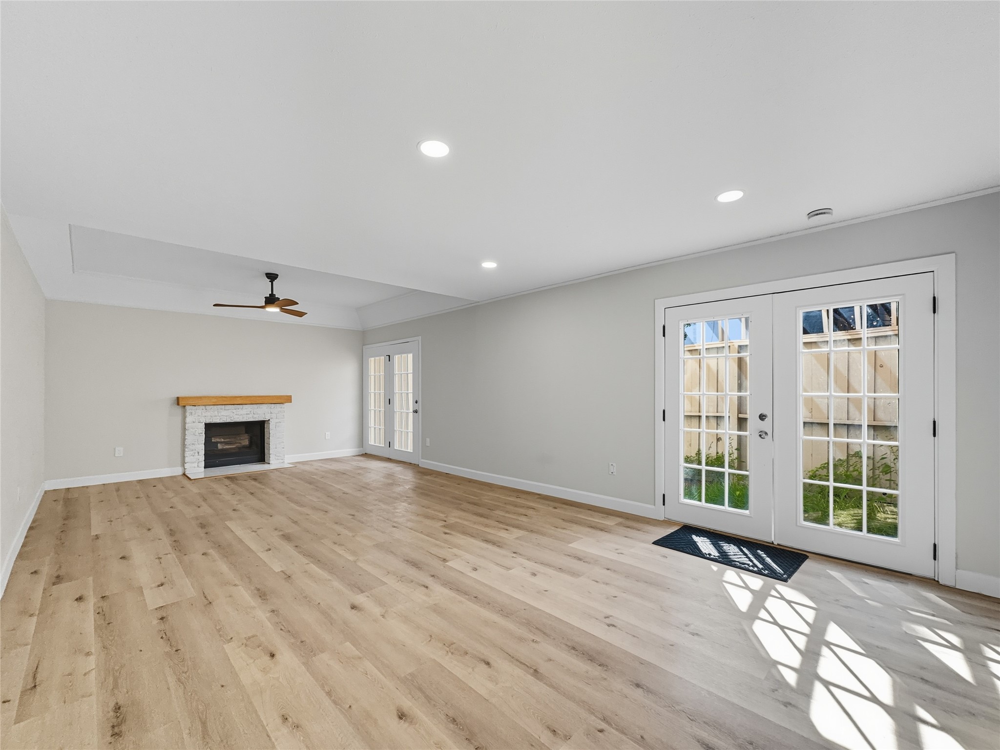 2243 West Alabama Street, Unit 10 Houston, TX 77098 - Photo 7 of 45 This spacious, bright living room features light wood flooring, a cozy white brick fireplace, and French doors leading to a fenced outdoor area. A ceiling fan and recessed lighting add modern comfort.