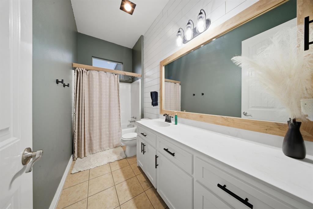 603 Cedar Drive Pilot Point, TX 76258 - Photo 24 of 39 Bathroom vanity with a white countertop and base cabinetry, featuring a large mirror with a natural wood-finish frame, a three-light fixture, and shiplap wall paneling