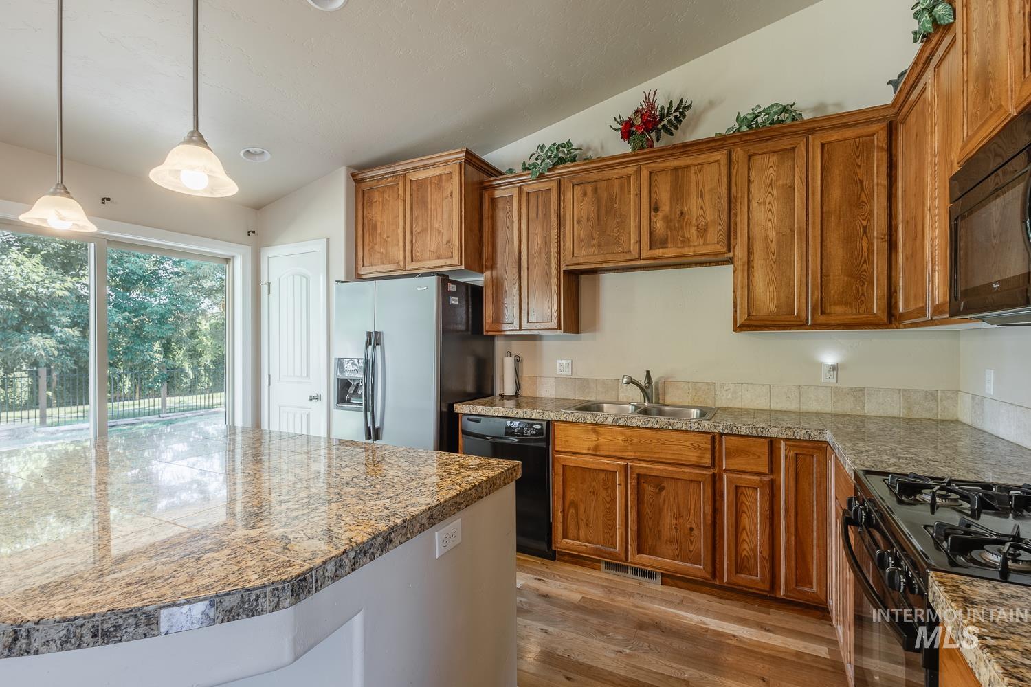 1186 East Observation Street Meridian, ID 83642 - Photo 13 of 33 Kitchen featuring granite countertops, wood cabinetry, stainless steel refrigerator, black range, and wood-finish flooring