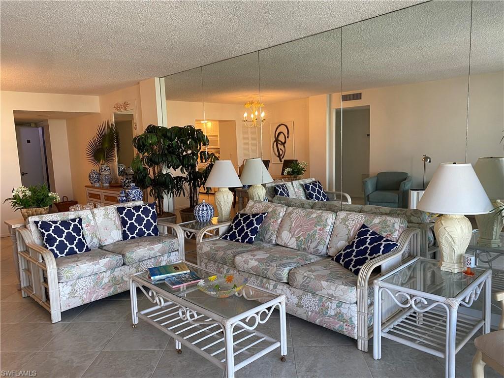 3 Bluebill Avenue, Unit 609 Naples, FL 34108 - Photo 13 of 15 Living room featuring a notable chandelier, tile patterned floors, and a textured ceiling