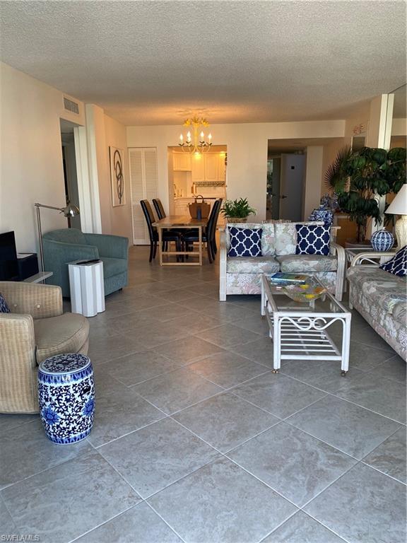 3 Bluebill Avenue, Unit 609 Naples, FL 34108 - Photo 4 of 15 Living room featuring an inviting chandelier and a textured ceiling
