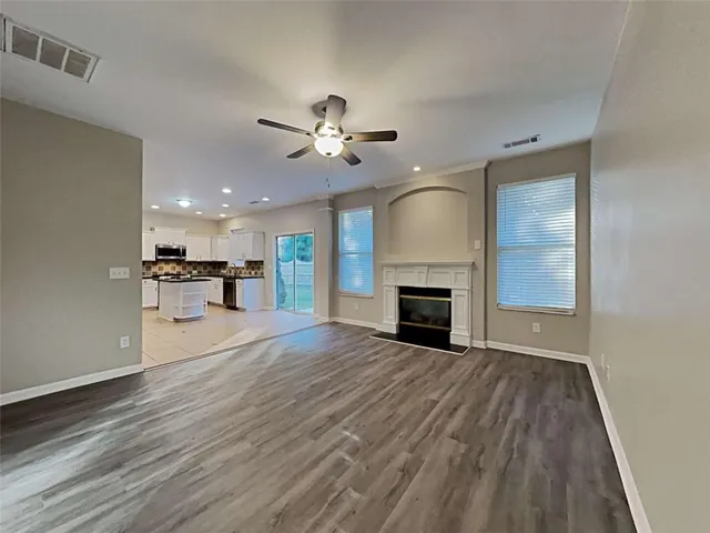 a view of a livingroom with a fireplace a ceiling fan a kitchen and chandelier