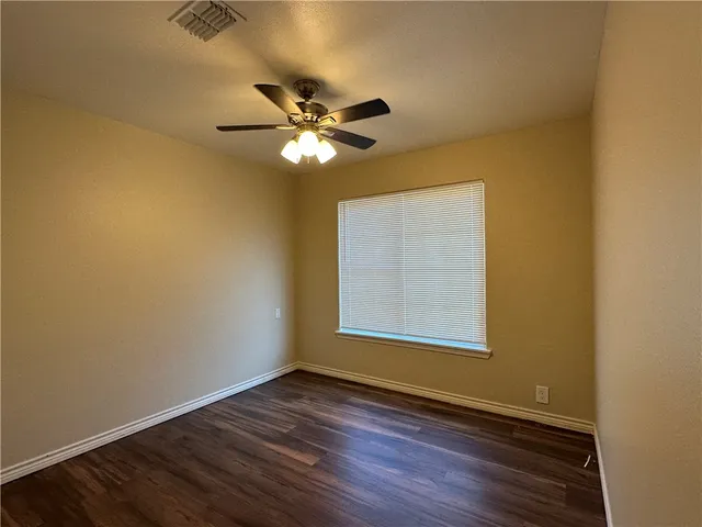 an empty room with wooden floor fan and windows