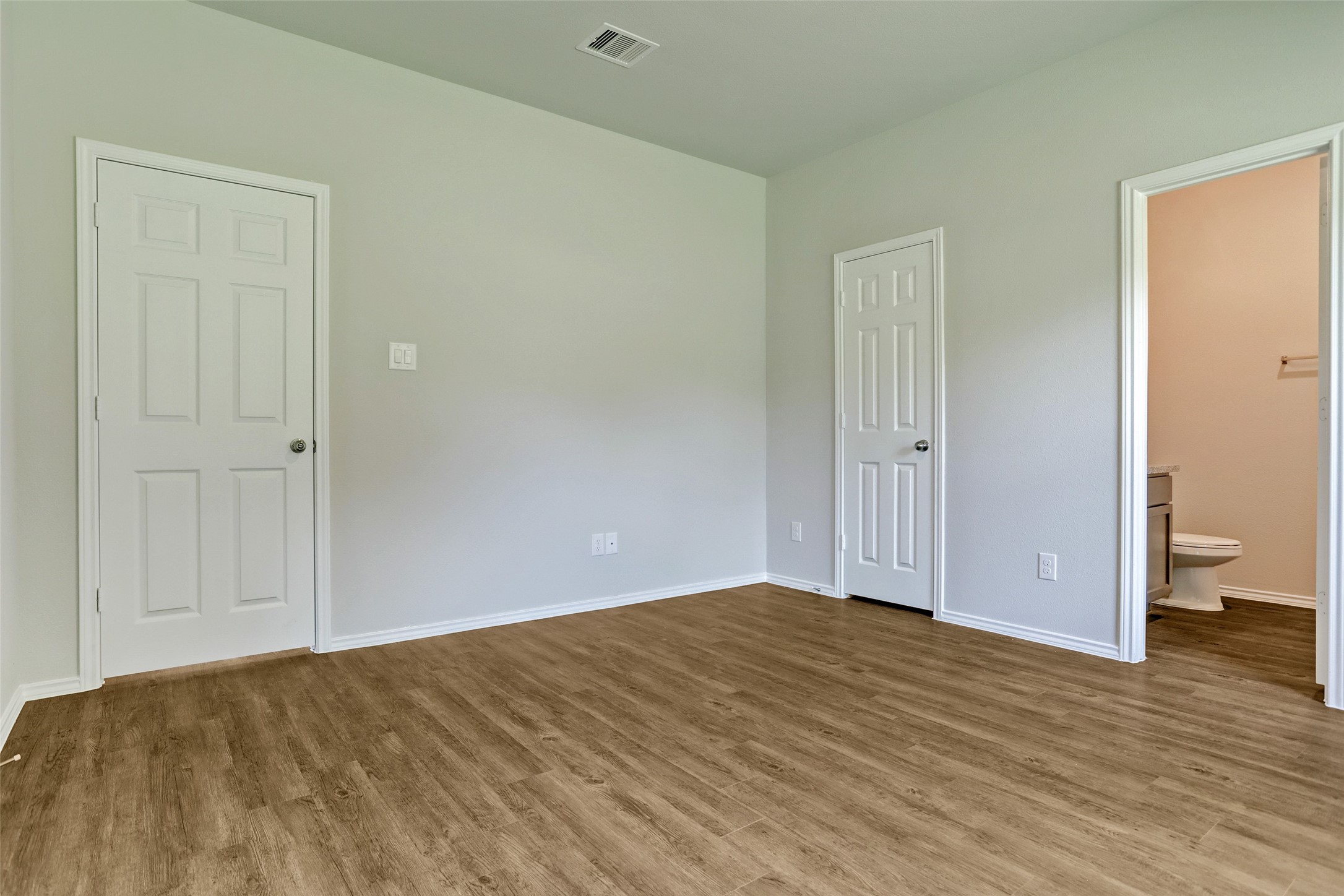 409 South 12th Street, Unit B Conroe, TX 77301 - Photo 11 of 14 This room features light-colored walls, wood-style flooring, and two white doors, one leading to an adjacent bathroom.