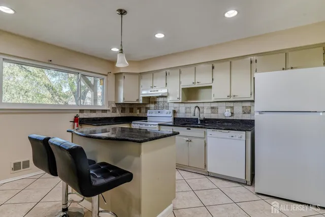a kitchen with stainless steel appliances granite countertop a sink a stove a refrigerator a microwave oven with white cabinets and wooden floor