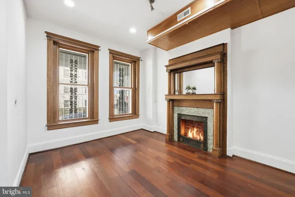 a view of an empty room with wooden floor fireplace and a window