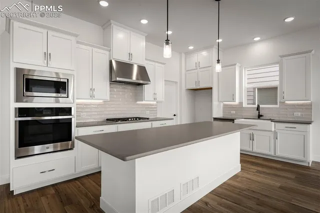 a kitchen with kitchen island granite countertop a stove a sink and white cabinets with wooden floor