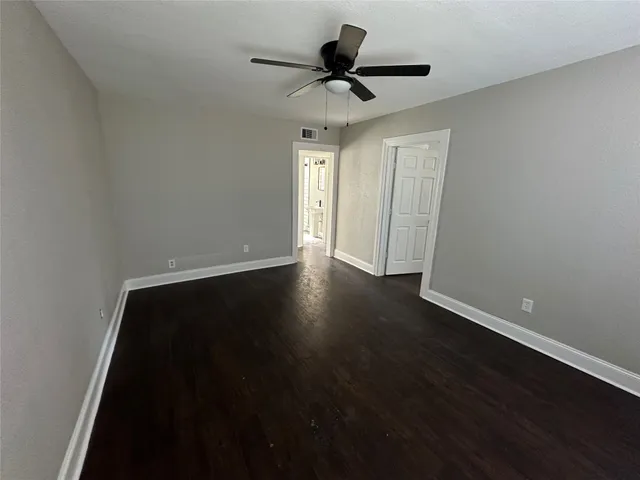 a view of an empty room with wooden floor and a ceiling fan