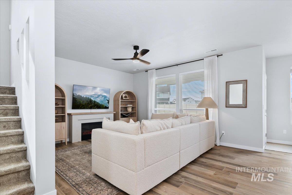 4215 North Pindus Avenue Meridian, ID 83646 - Photo 13 of 46 Living area with LVP floors, a ceiling fan, and picture windows. Carpeted 180-degree stairway.