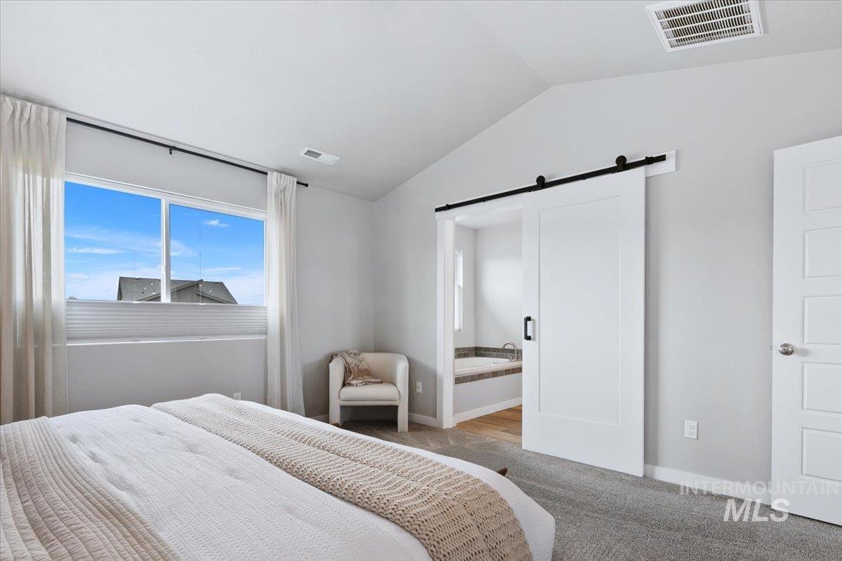 4215 North Pindus Avenue Meridian, ID 83646 - Photo 24 of 46 Bedroom featuring vaulted ceiling, a barn door, connected bathroom, and light colored carpet