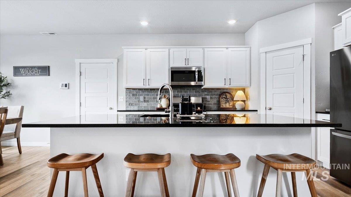 4215 North Pindus Avenue Meridian, ID 83646 - Photo 7 of 46 Kitchen with island seating for four, LVP flooring, white cabinetry, stainless steel appliances