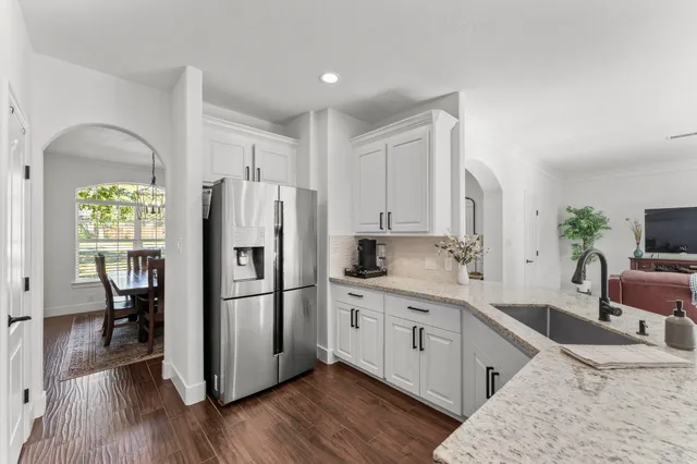 a kitchen with stainless steel appliances granite countertop a refrigerator a sink dishwasher and white cabinets with wooden floor