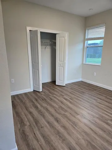 an empty room with wooden floor closet and windows