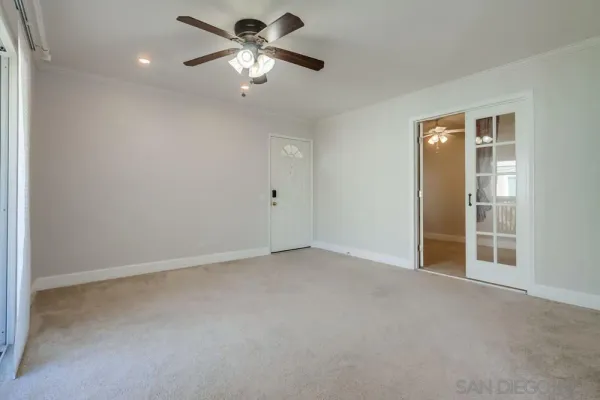an empty room with chandelier fan and windows