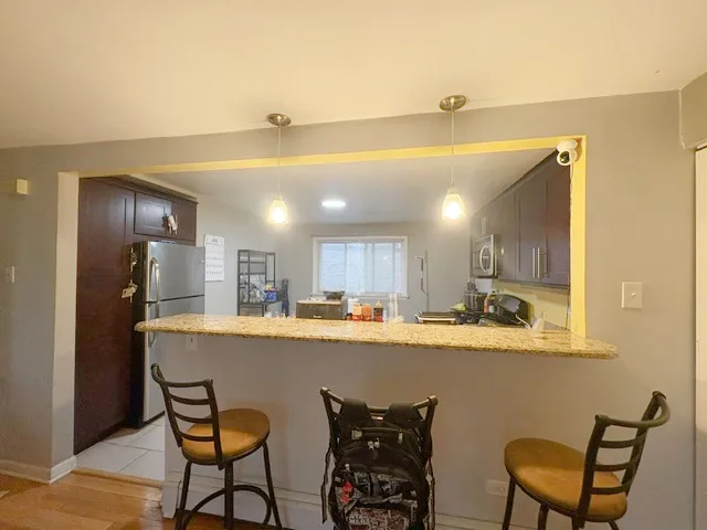 a room with stainless steel appliances kitchen island granite countertop a dining table chairs and a refrigerator