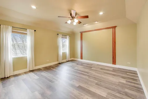 a view of an empty room with wooden floor and a ceiling fan