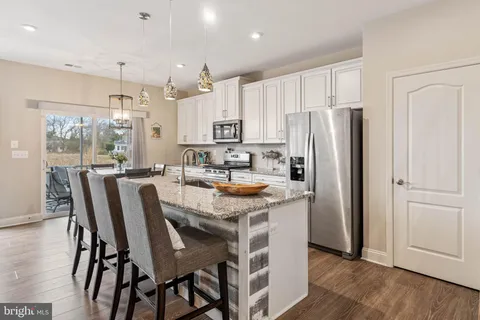 a kitchen with stainless steel appliances granite countertop a dining table chairs refrigerator and cabinets