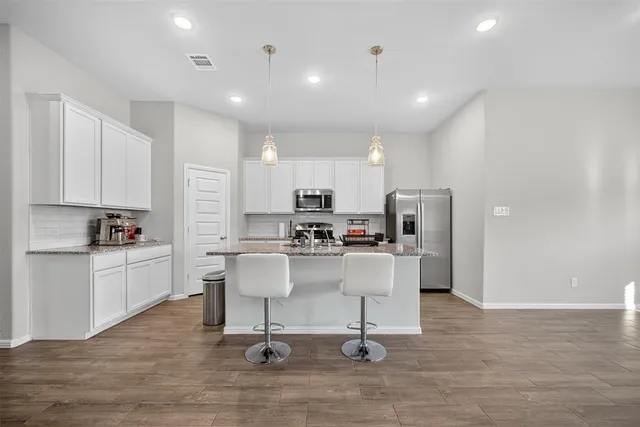 a kitchen with stainless steel appliances granite countertop a refrigerator a stove top oven a sink dishwasher and white cabinets with wooden floor