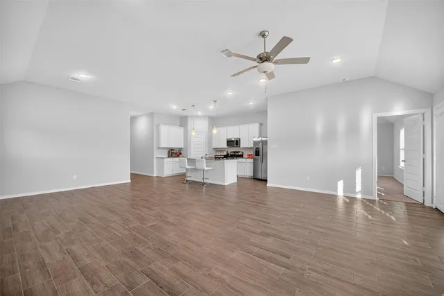 a view of an empty room and kitchen with wooden floor