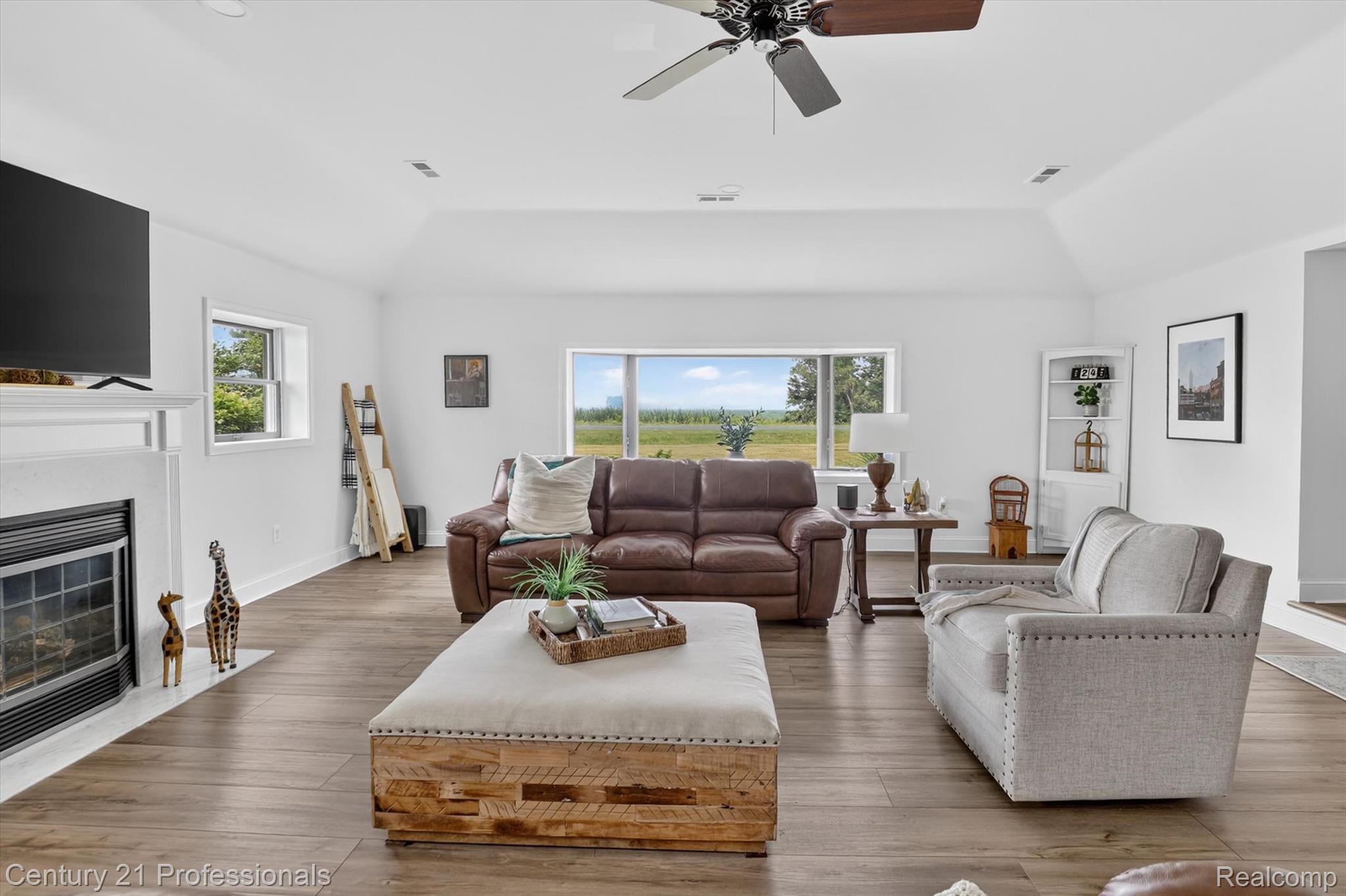13525 Dennison Road Milan, MI 48160 - Photo 16 of 69 Spacious living area featuring a vaulted ceiling with a fan, a white mantel fireplace, large windows, and wood-finish flooring