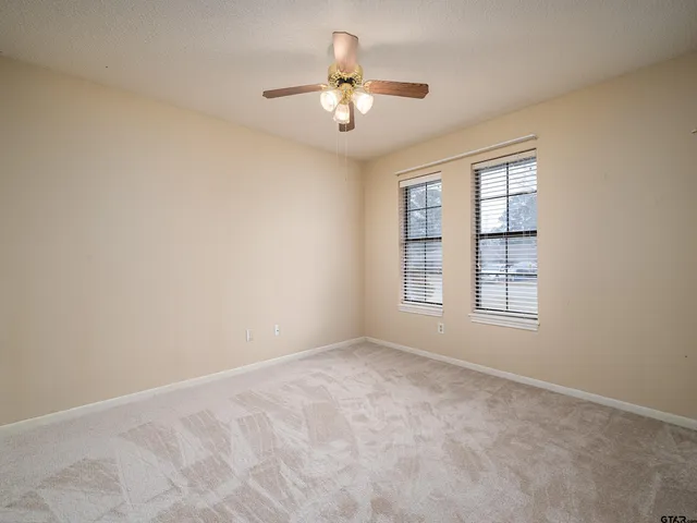 an empty room with chandelier fan and windows