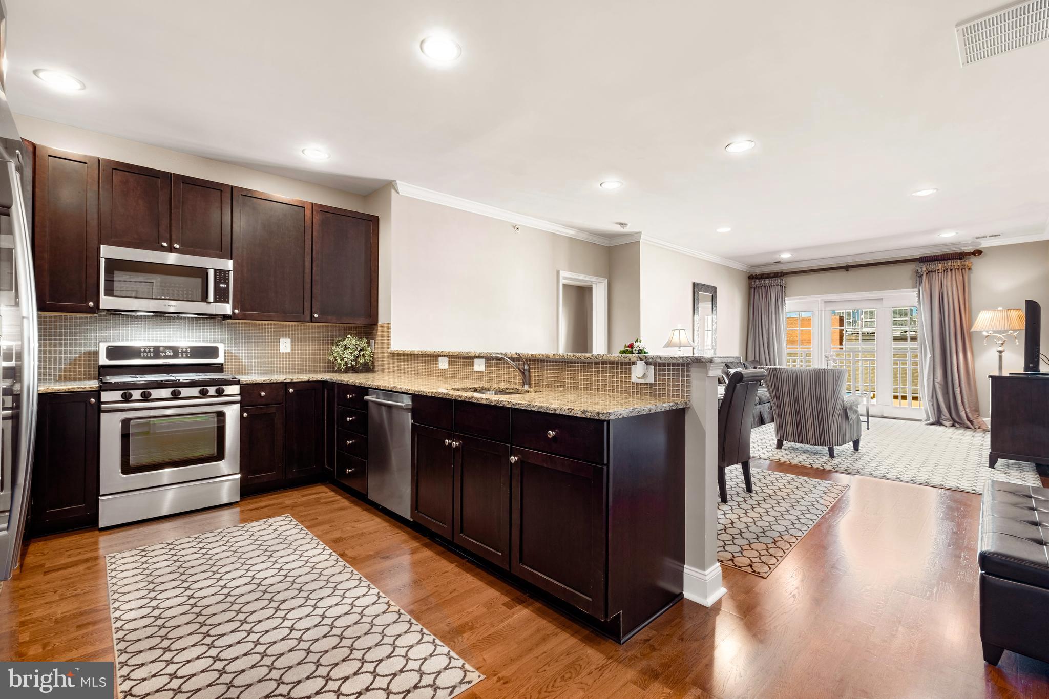 a kitchen with stainless steel appliances granite countertop a stove top oven a sink dishwasher a refrigerator and a dining table with wooden floor