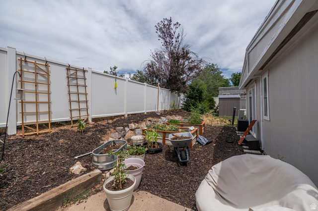 2600 North Hill Field Road, Unit 5 Layton, UT 84041 - Photo 22 of 33 Landscaped backyard featuring a white vinyl privacy fence, a raised garden bed, and a detached storage shed