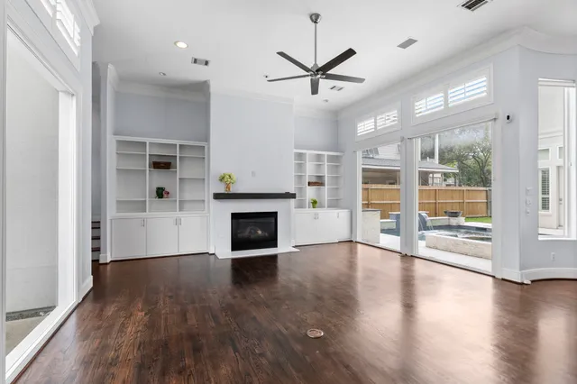 an empty room with wooden floor a ceiling fan and windows