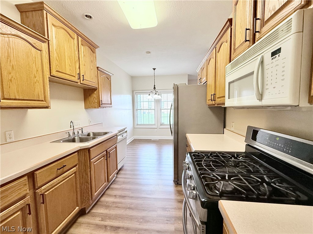 603 South Raccoon Road, Unit 1 Austintown, OH 44515 - Photo 6 of 22 Galley kitchen featuring wood cabinetry, stainless steel sink, wood-finish flooring, and a full suite of appliances including a range and microwave