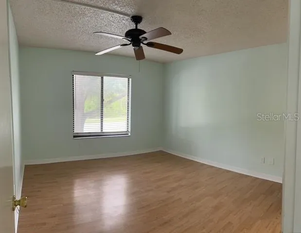 an empty room with wooden floor fan and windows