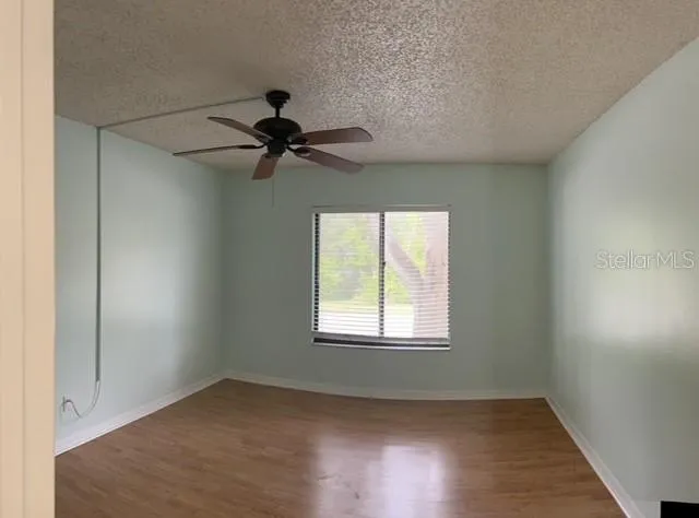 an empty room with wooden floor ceiling fan and windows