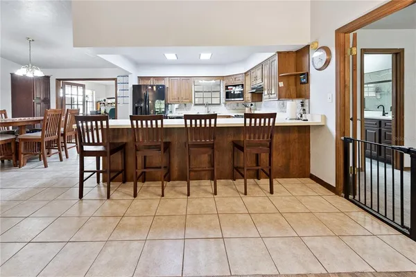 a dining hall with stainless steel appliances kitchen island granite countertop a refrigerator a stove a dining table and chairs with wooden floor