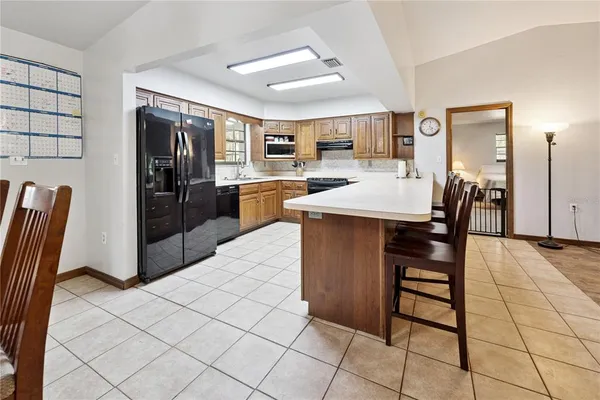 a dining hall with stainless steel appliances kitchen island granite countertop a refrigerator a stove a sink with island and chairs