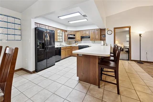 a dining hall with stainless steel appliances kitchen island granite countertop a refrigerator a stove a sink with island and chairs