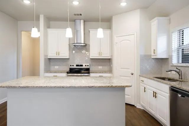 a kitchen with stainless steel appliances granite countertop a sink a refrigerator a center island a stove and white cabinets