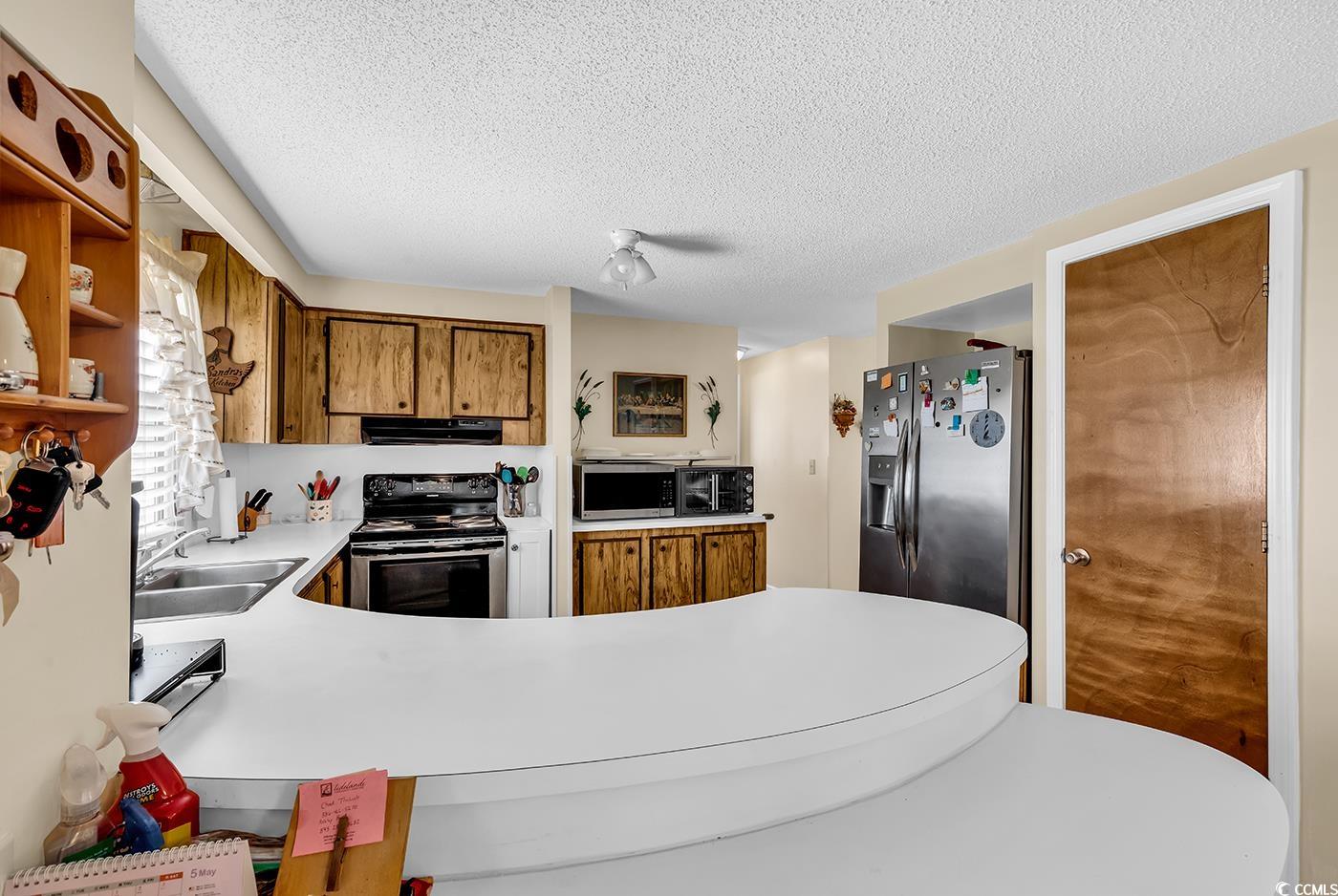 449 Rainbow Drive Murrells Inlet, SC 29576 - Photo 6 of 33 Kitchen with brown cabinetry, light countertops, a textured ceiling, stainless steel appliances, and a peninsula