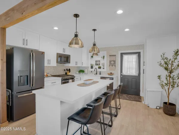 a kitchen with stainless steel appliances a refrigerator a sink a stove and chairs with wooden floor