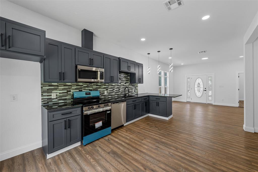 2023 Bosque Boulevard Waco, TX 76707 - Photo 9 of 26 Modern kitchen featuring dark cabinetry, stainless steel appliances, a mosaic tile backsplash, and sleek pendant lighting